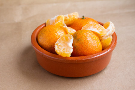 Tangerines and peeled slices elegantly displayed in a brown ceramic bowl. Ideal for concepts such as healthy eating, fresh produce, citrus fruits, and nutrition. Bright and eye-catching presentation.の写真素材