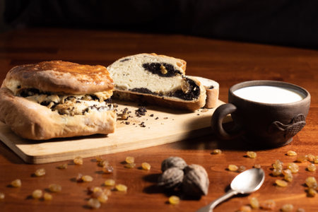 Freshly baked bread and pastry complemented by raisins, nuts, and milk, creating a hearty rustic scene. Wooden surface highlights the natural aesthetic of the food arrangement.の写真素材