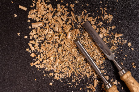 two wooden-handle chisels with wooden chips and sawdust on a black speckled background top view