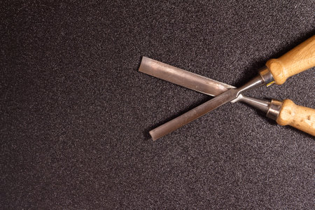 Two metal woodworking chisels with wooden handles displayed on a textured black surface.の写真素材