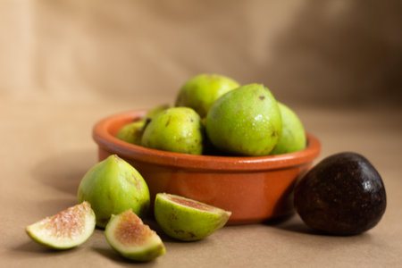 Ripe green figs and a dark avocado placed in a ceramic bowl, with some figs sliced, creating a...