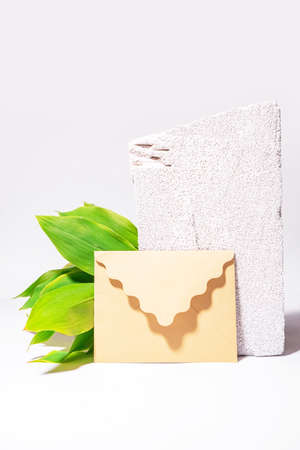 Natural background with craft envelope, green leaves and white textured stone. Still life wallpaper....