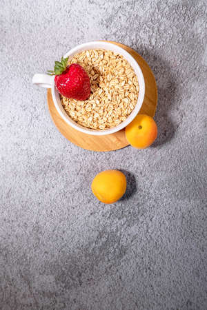 Healthy breakfast with bowl of oat, strawberry and apricot on concrete background. Space for text....