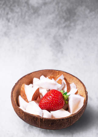 A bowl of coconut pieces and strawberry on concrete background. Coconut ingredient on plate. Vegan...