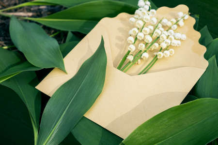Craft envelope mockup with lily of the valley flower and green leaves on nature ground. May-lily in...
