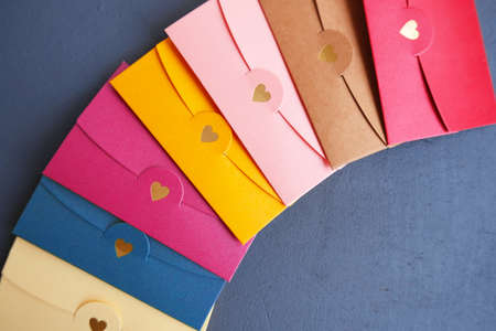 Stack of yellow, red, blue, pink, brown, beige envelope on dark gray background. Valentines Day greeting banner. Trendy minimal poster for 14 February. Wedding invitation. Dating message. Guest cardの写真素材