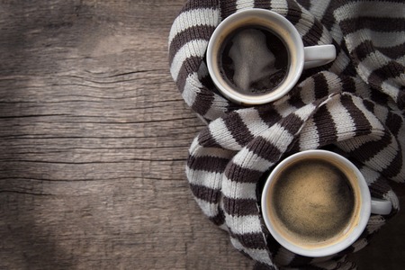 two mugs of hot coffee with foam standing on a wooden background wrapped in warm knit wool striped scarf. the view from the top. space for text. the concept of heat. copyspace.の写真素材