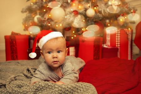 Cute little baby girl lying next to the Christmas tree in Room decorated on Christmas. Merry...