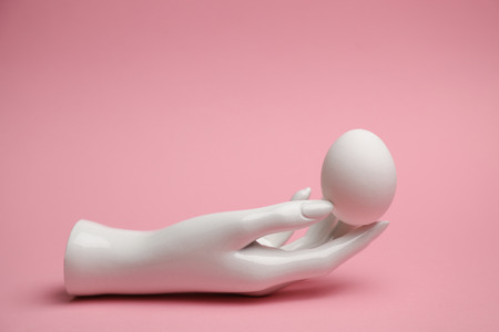 Easter white egg in the white hand of the dummy on a pink backgrの写真素材