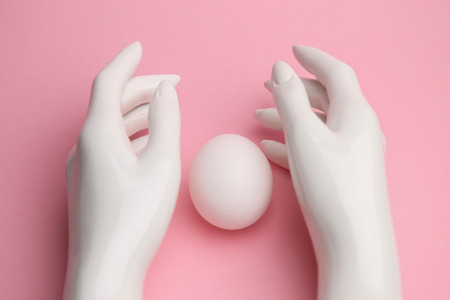 a mannequin hand on a pink background about white chicken egg. the concept of Easter and religion.の写真素材