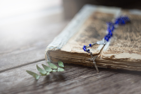 Cross on the antique Bible on a wooden table background. Holy book.