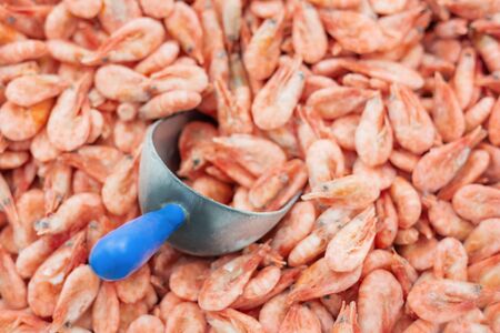 Pink fresh frozen shrimps with ice and filling scoop in a supermarket or fish shop. Uncooked seafood...