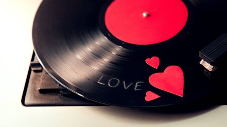 Retro record player with a black vinyl record with a red heart and the inscription love closeup with a place for text.の写真素材