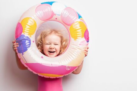 little Caucasian girl in a pink swimsuit with a rubber ring on a white background. summer vacation with children conceptの写真素材