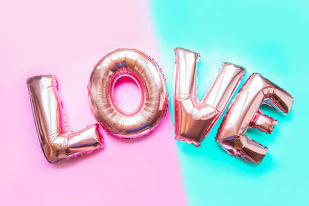 pink letter-shaped balloons forming the word love on pink and blue background,