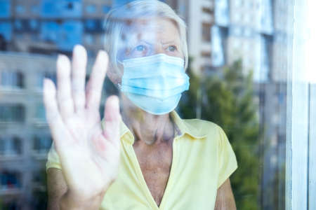 Elderly caucasian women wearing protective face mask, in home, looking outside window. Old lady...