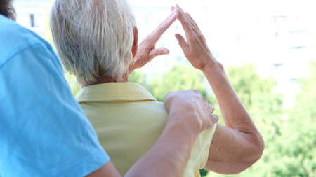 Caucasian young son embracing elderly mother chooses house back view. real estate deal concept.の写真素材