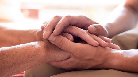 Worried caucasian man gently stroking hand of his sick old mother showing care or love. Son comforting wrinkled arm of elderly mom sitting at bed. Guy giving support to his old parent slow motion.の写真素材