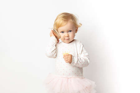 funny angry curly caucasian baby girl with a mobile phone in her hands with a serious face on a white background with copy space. concept bad cellular connection.の写真素材