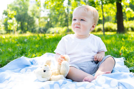 portrait of a baby boy sitting on green grass in the park on a blanket on a summer sunny day. concept of walking with childrenの写真素材
