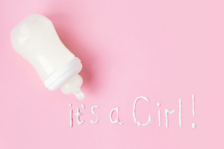 plastic baby bottle on a pink background with spilled milk