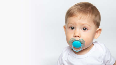Charming baby boy child 7 month old sucks a pacifier on white background. toddler with dummy in...