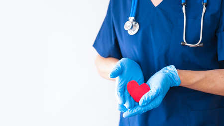 hands of a male doctor dressed in medical blue gloves hold a red heart close-up. medical banner with copy space for text. healthcare concept.の写真素材