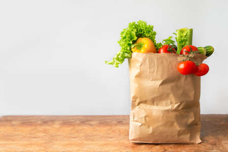 Healthy vegan vegetarian food in paper bag vegetables on white and wooden background. copy space, banner. Healthy food delivery background. Shopping supermarketの写真素材