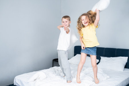Boy and girl playing in parents bed. family morning. Small children laughing and jumping on a bed and having fun. Indoor positive activity. cheerful siblings Kids have free timeの写真素材