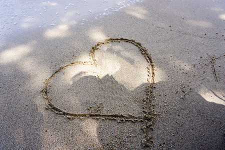 hand writing heart symbol on the sand. valentine day or love conceptの写真素材