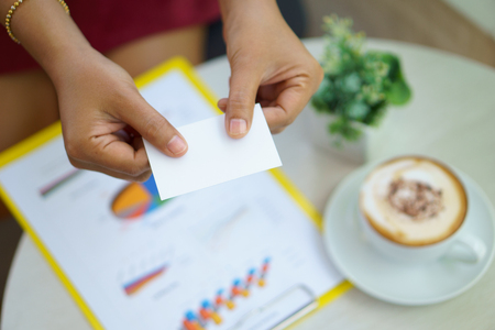 close up of young business women two hand giving or exchange white name card over business document and latte art during business meeting agreement and contractの写真素材