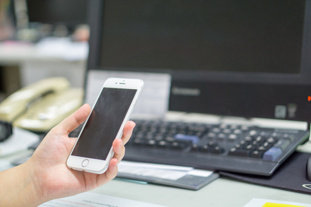 young business women right hand holding smart phone with all in one computer backgroundの写真素材