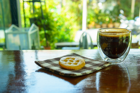 espresso coffee in transparent cup with cookies on piece of cloth on the wooden table near window.の写真素材