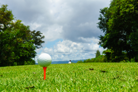 close up of white golf ball on orange tee at tee off with golf course background and blue sky and cloud at mae moh golf course hole 1, down hill layout, lampang, thailand. copy space for your text.の写真素材