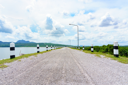 Crushed rock road along the dam with cloudy sky. mile stone abstract concept.の写真素材