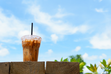 close up of iced latte coffee in transparent plastic glass and straw with on the wooden table with blue sky and cloud. coffee and cafe concept.の写真素材