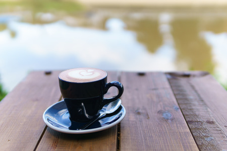 close up of hot latte in dark blue cup with spoon on the wooden table near the river. copy space for your text.の写真素材