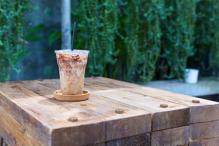 iced latte coffee in transparent plastic cup with black straw in coaster on the vintage wooden table with copy space for text. coffee concept.の写真素材