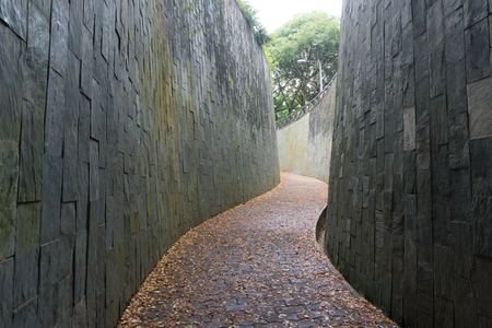 redbrick pathway or footpath with big stone wall in sunny day. underground crossing at fort canning public park,singapore. travel concept.のeditorial素材