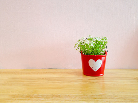 small mock up or fake plant in the red pot with white heart sign on the wooden table with pink wall background.の写真素材