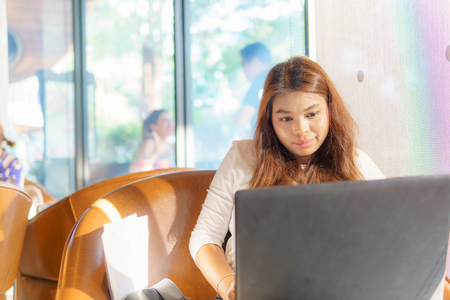 beautiful asian young business woman sitting near transparent window with business document and laptop for her job at cafe or coffee shop. business success concept.の写真素材
