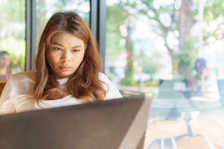 beautiful asian young business woman sitting near transparent window with laptop for her job and feeling stress at cafe or coffee shop. business success concept.の写真素材