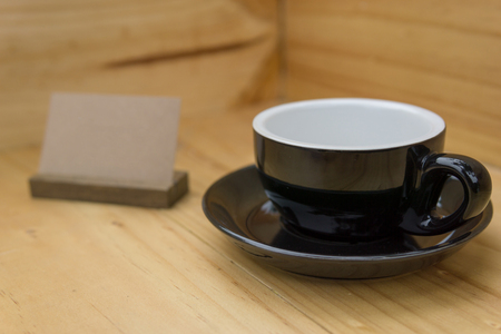 selective focus, close up of empty black coffee cup on the corner of wooden room or box with brown stand label. food or interior concept.の写真素材