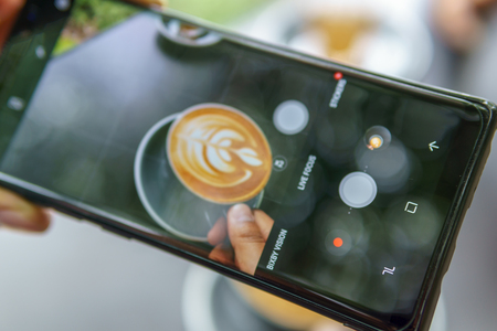 close up of smartphone taking photo of hand holding cup of latte art coffee.の写真素材