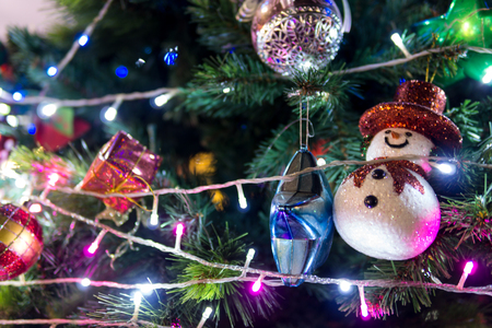 Selective focus. close up of beautiful decorated christmas ball and snowman doll on the green tree with light at night. copy space for text. xmas or new year concept.の写真素材