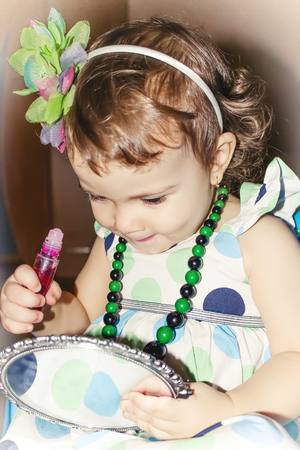 Beautiful little girl looking in the mirror and paints her lips.の写真素材