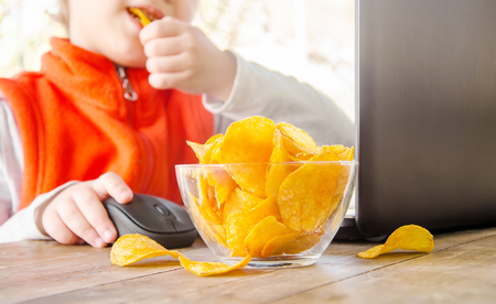 child with chips behind a computer. selective focus. food.の写真素材