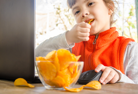 child with chips behind a computer. selective focus. food.の写真素材