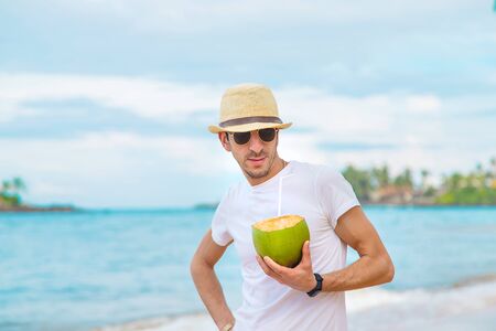 A man on the beach drinks coconut. Selective focus.