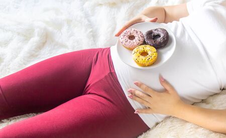 A pregnant woman eats sweet donuts. Selective Focus. Food.の写真素材